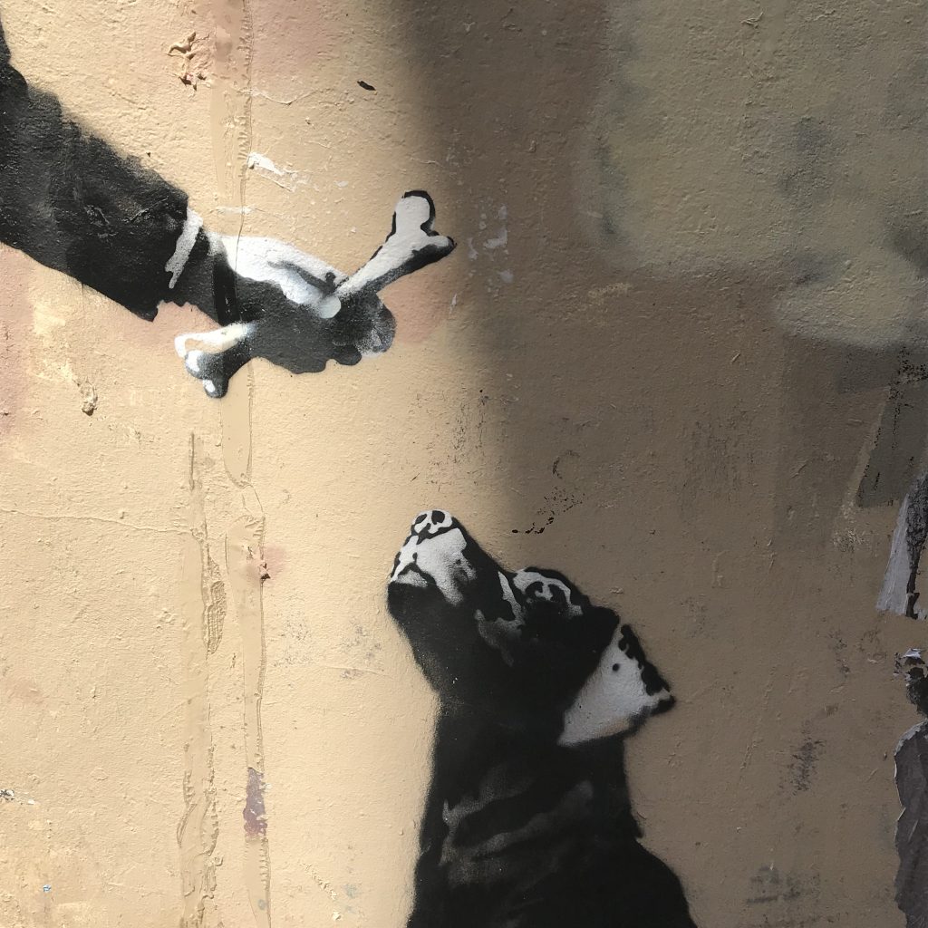 Detailed view of Banksy’s Businessman with a Saw mural, highlighting the three-legged dog and the bone offered by the businessman near the Sorbonne.