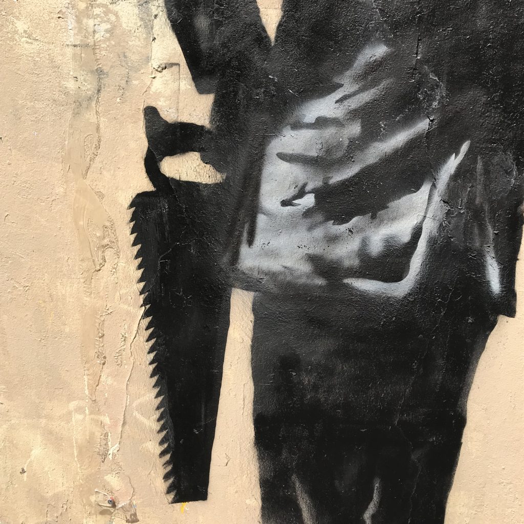 Close-up of Banksy’s Businessman with a Saw mural, focusing on the saw hidden behind the figure’s back near the Sorbonne University.