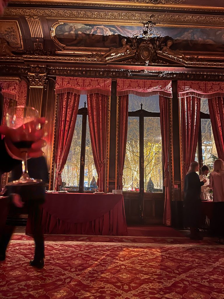 Interior view of the dining room at the Travellers Club in Paris, featuring elegant décor and a stunning view of the illuminated Champs-Élysées through the windows.