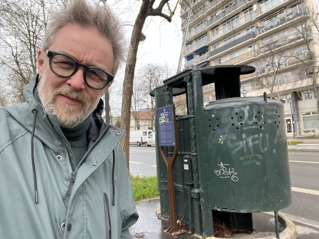 Yours truly standing beside the 19th-century pissoir at Boulevard Arago in Paris, showcasing its historical charm.