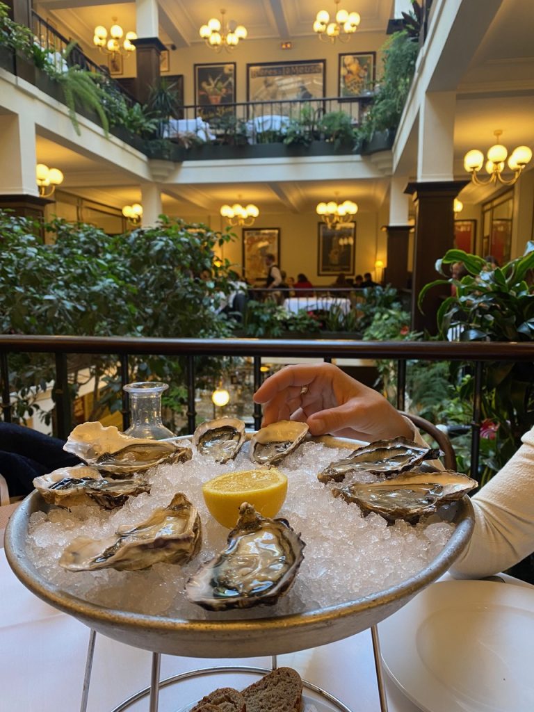 Plate of fresh oysters served at Café du Commerce in Paris, accompanied by lemon wedges and a glass of white wine.