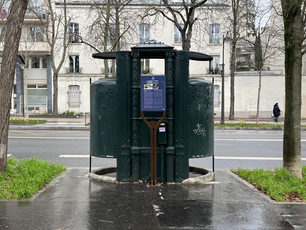 Exterior view of the 19th-century pissoir at Boulevard Arago in Paris, showcasing its classic cylindrical design and perforated iron panels.