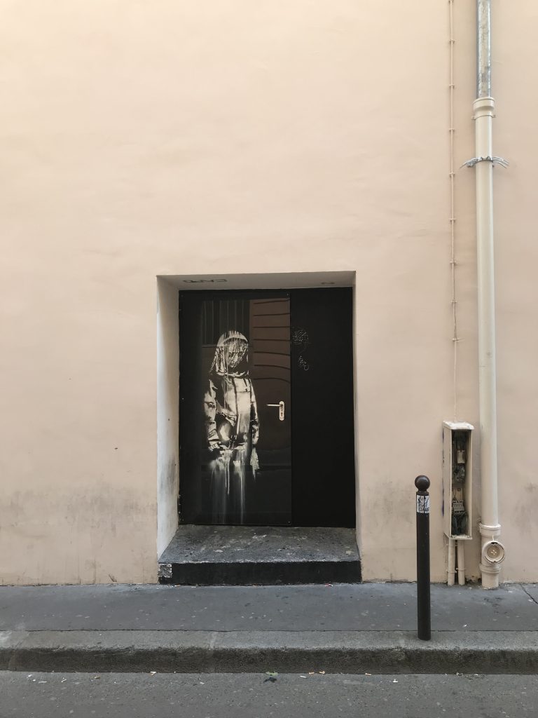 Distant view of Banksy’s The Mourning Figure mural outside the Bataclan, showing the veiled figure bowing her head in a solemn pose.